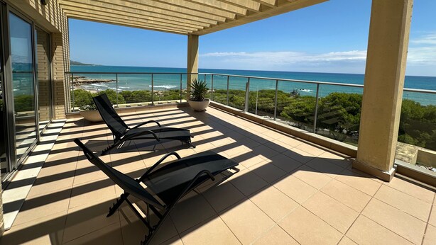 Een balkon met twee zwarte ligstoelen, een potplant en uitzicht op de oceaan.
