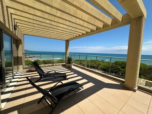 A balcony with two black lounge chairs, a potted plant, and a view of the ocean. - Alcocebre Suites Hotel (Alcala de Xivert)