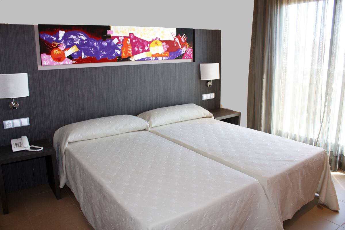 Hotellihuone, jossa on parivuode, yöpöytä, jossa on puhelin, ja seinälle kiinnitetty taideteos.