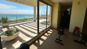 Een ruim balkon met vrij uitzicht op zee, een grote potplant en fitnessapparatuur.
