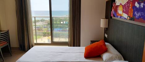 Hotelkamer met een groot bed, twee kussens, een nachtkastje, een lamp en uitzicht op het strand en het resort.