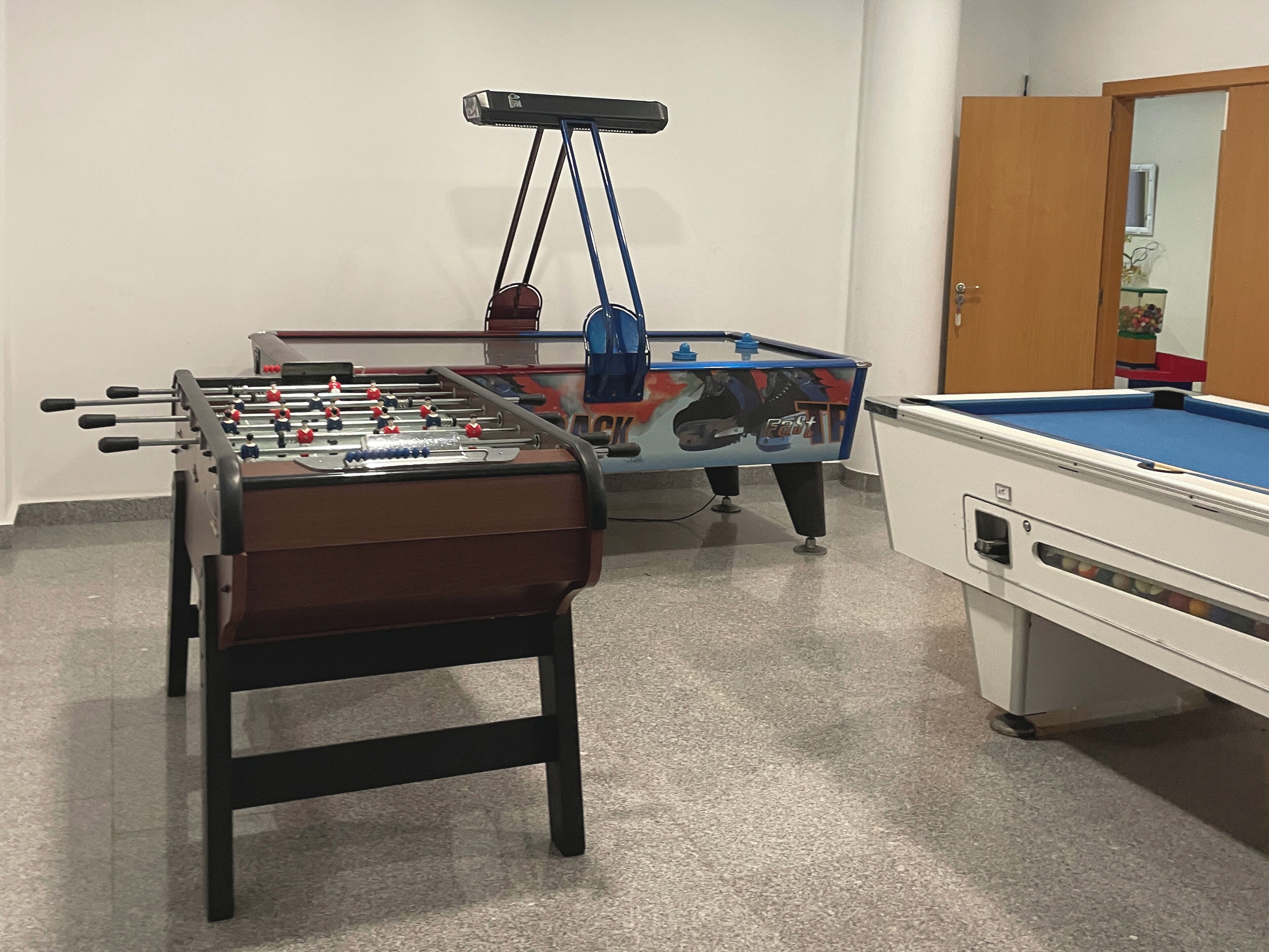 A room with a foosball table, a pool table, and a cabinet.