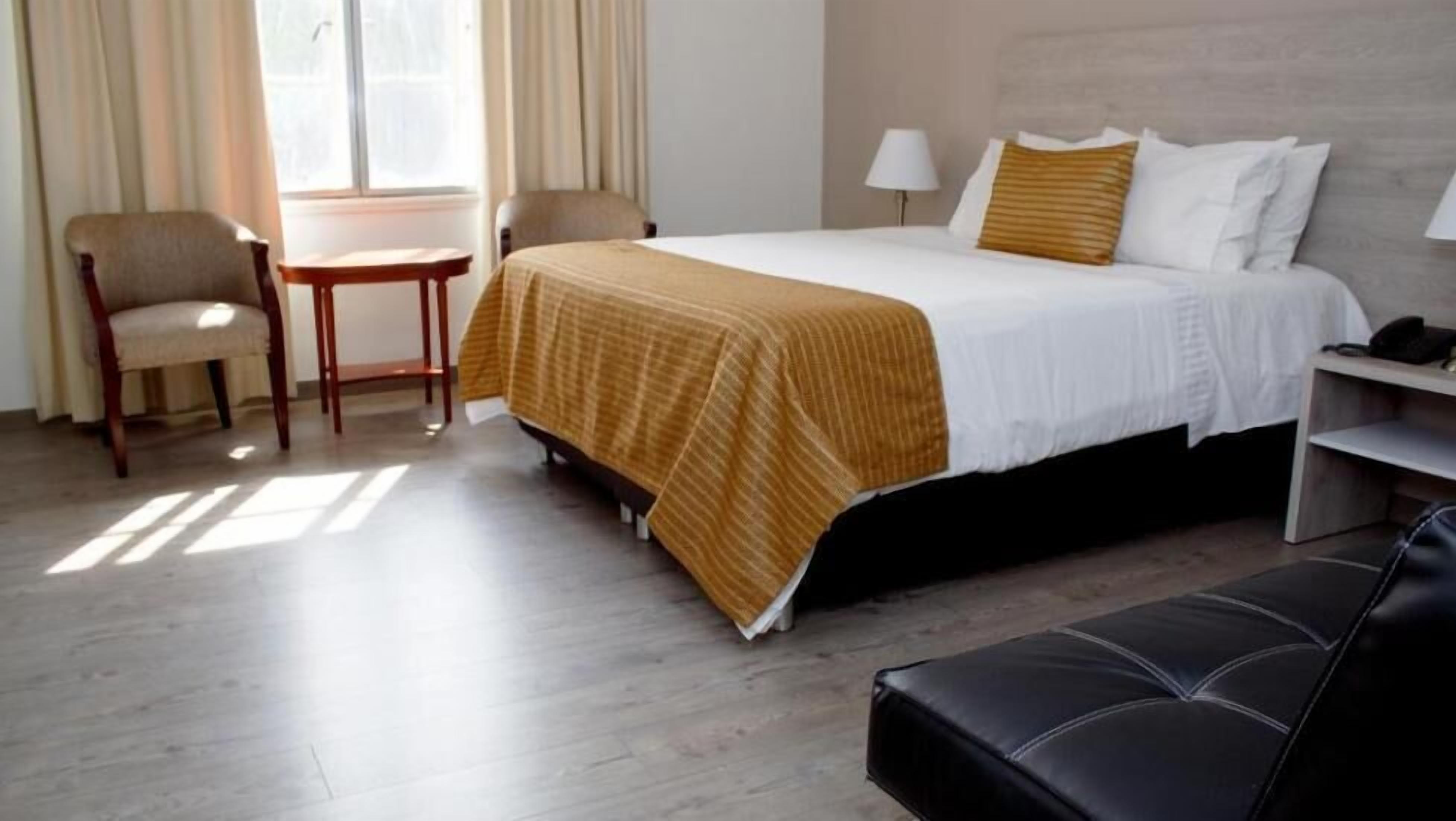 A hotel room with a bed, two chairs, a small table, and a lamp.