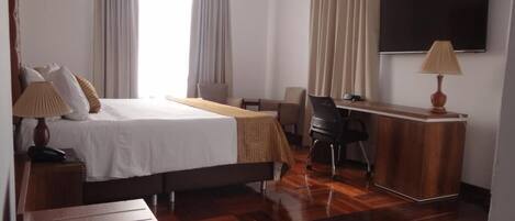 A hotel room with a bed, a desk, a chair, a TV, and a lamp.
