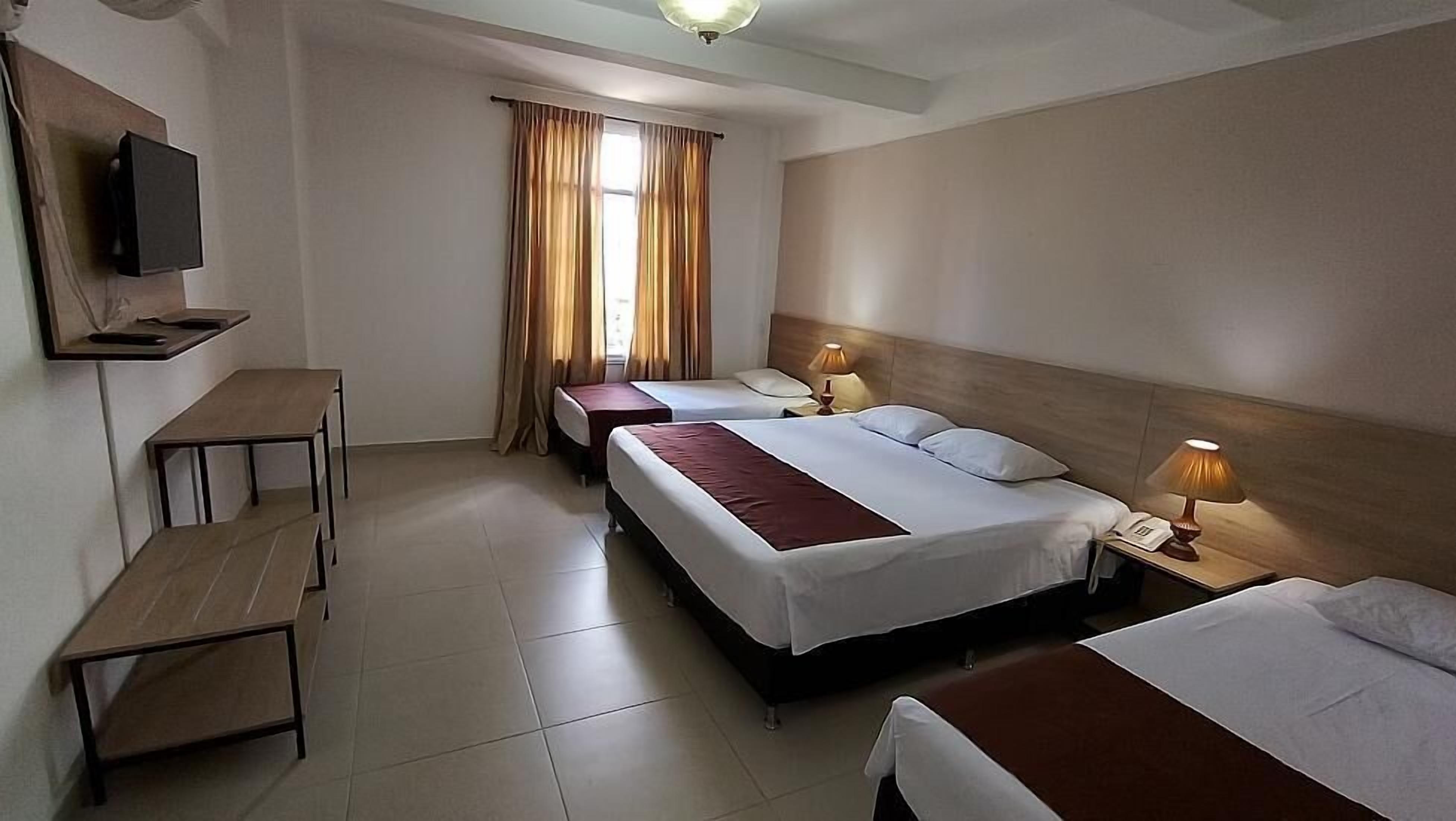 A hotel room with two beds, a desk, a television, and a window with curtains.