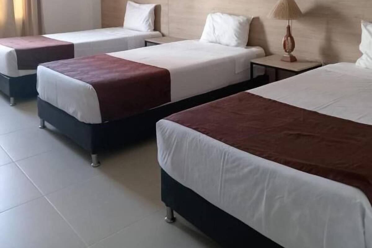 A hotel room with three single beds, a small table, and a lamp.