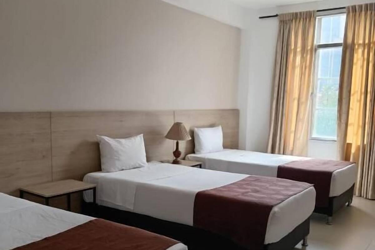 A hotel room with three beds, a ceiling fan, and a window with curtains.