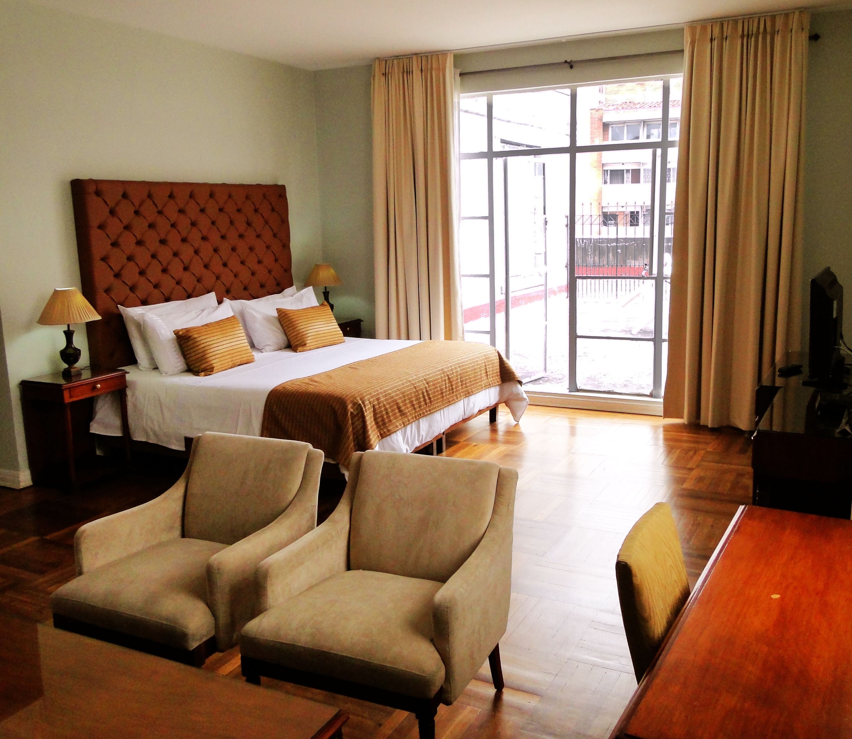 Ein Hotelzimmer mit einem großen Bett, zwei Sesseln, einem Holztisch und einem Fernseher.