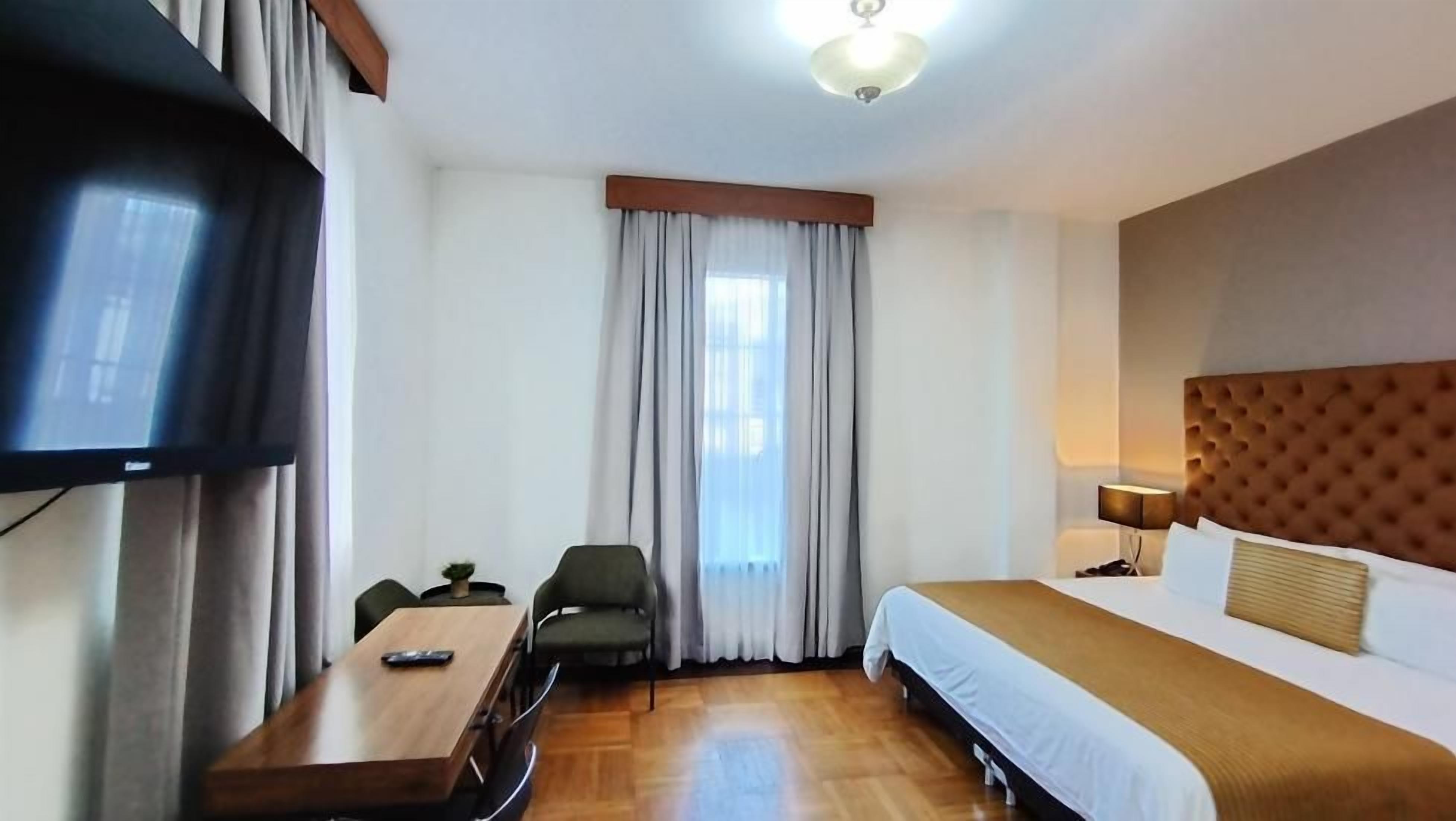 A hotel room with a bed, a desk, a chair, a television, and a window with curtains.