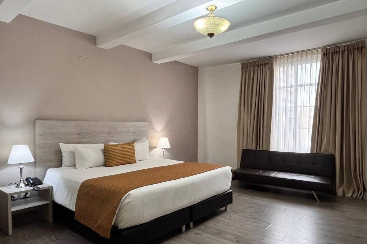 A hotel room with a large bed, bedside lamps, a TV, and a wooden floor.