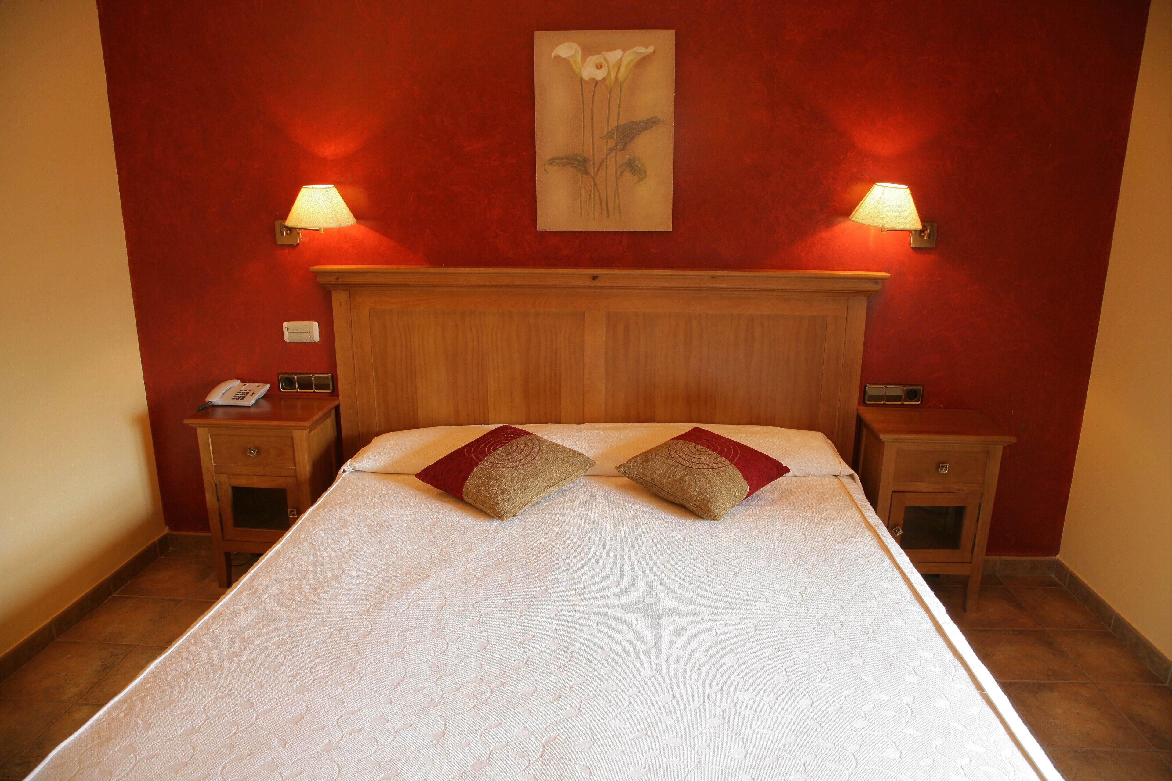 Habitación de hotel con una cama grande, dos mesitas de noche, un cabecero de madera y dos lámparas fijadas a la pared.