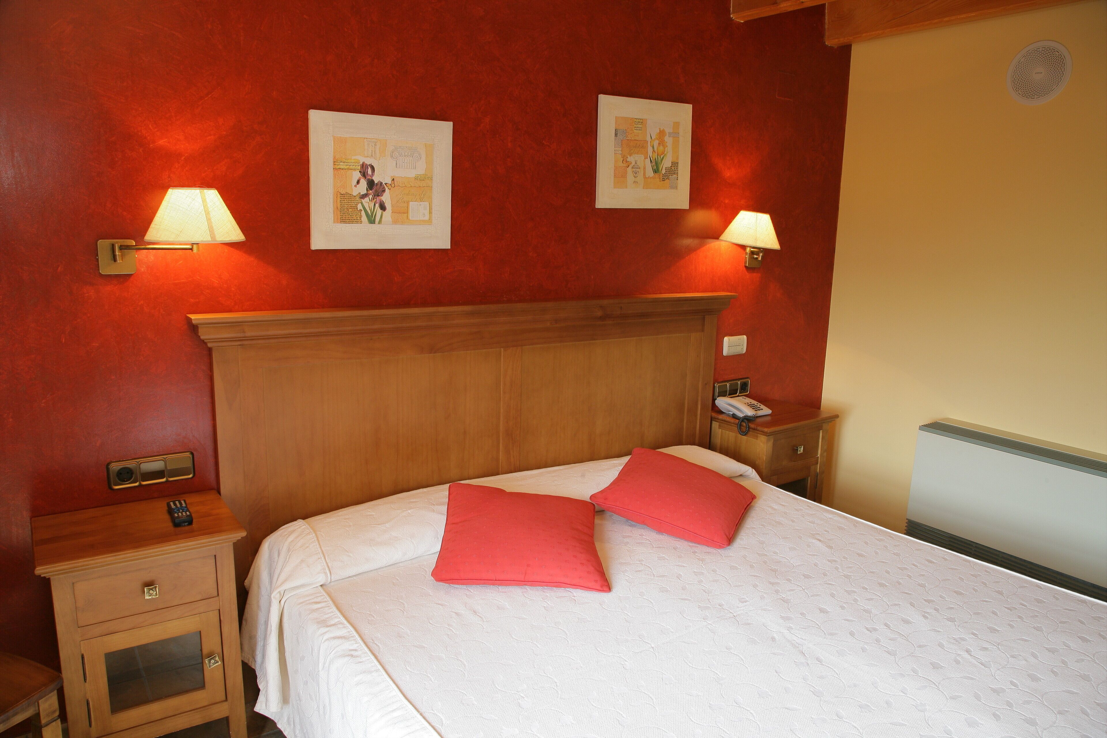 A neatly made bed with two red pillows, a wooden headboard, and two bedside tables with lamps.