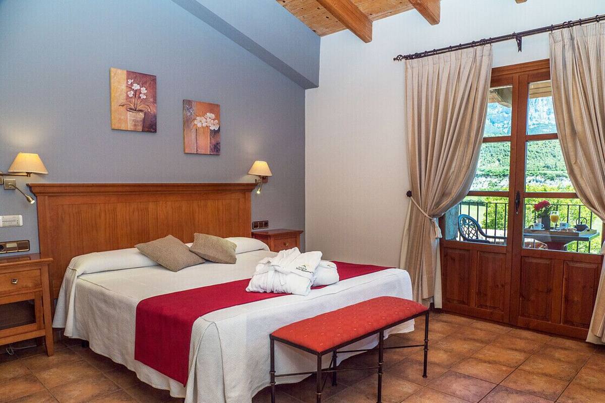 Un dormitorio con cama, un banco, una mesita de noche, una lámpara y una ventana con cortinas.