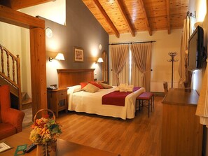 A hotel room with a wooden ceiling, a bed with a red blanket, a bedside table with a lamp, a chair, and a wooden desk with a television. - Hotel & Spa Peña Montañesa (Labuerda)