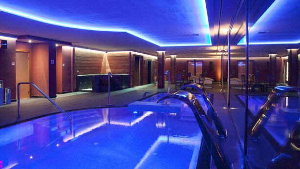 A modern indoor pool area with clear pool lines, a seating area, and a reception desk.