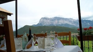 A dining table set with glasses, plates, and a bottle, overlooking a mountainous landscape.