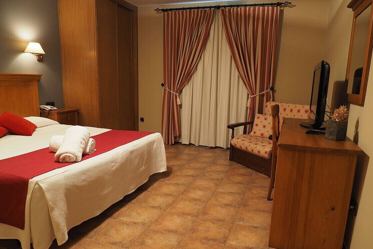 Habitación de hotel con cama, una silla, escritorio, lámpara, cortinas y un espejo.