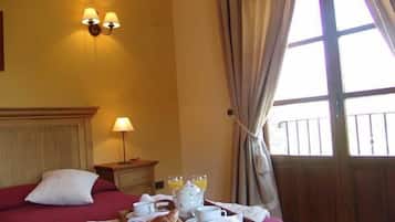 Habitación de hotel con cama, mesita de noche y bandeja de desayuno con croissants, té y jugo.