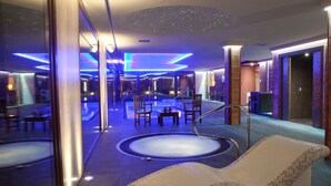 A modern spa area with a large hot tub, lounge chairs, and a glass-enclosed pool.