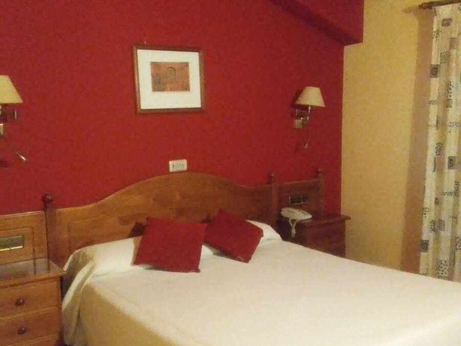 Habitació d'hotel amb un llit de fusta, panells vermells i dues taules de nit amb làmpades.