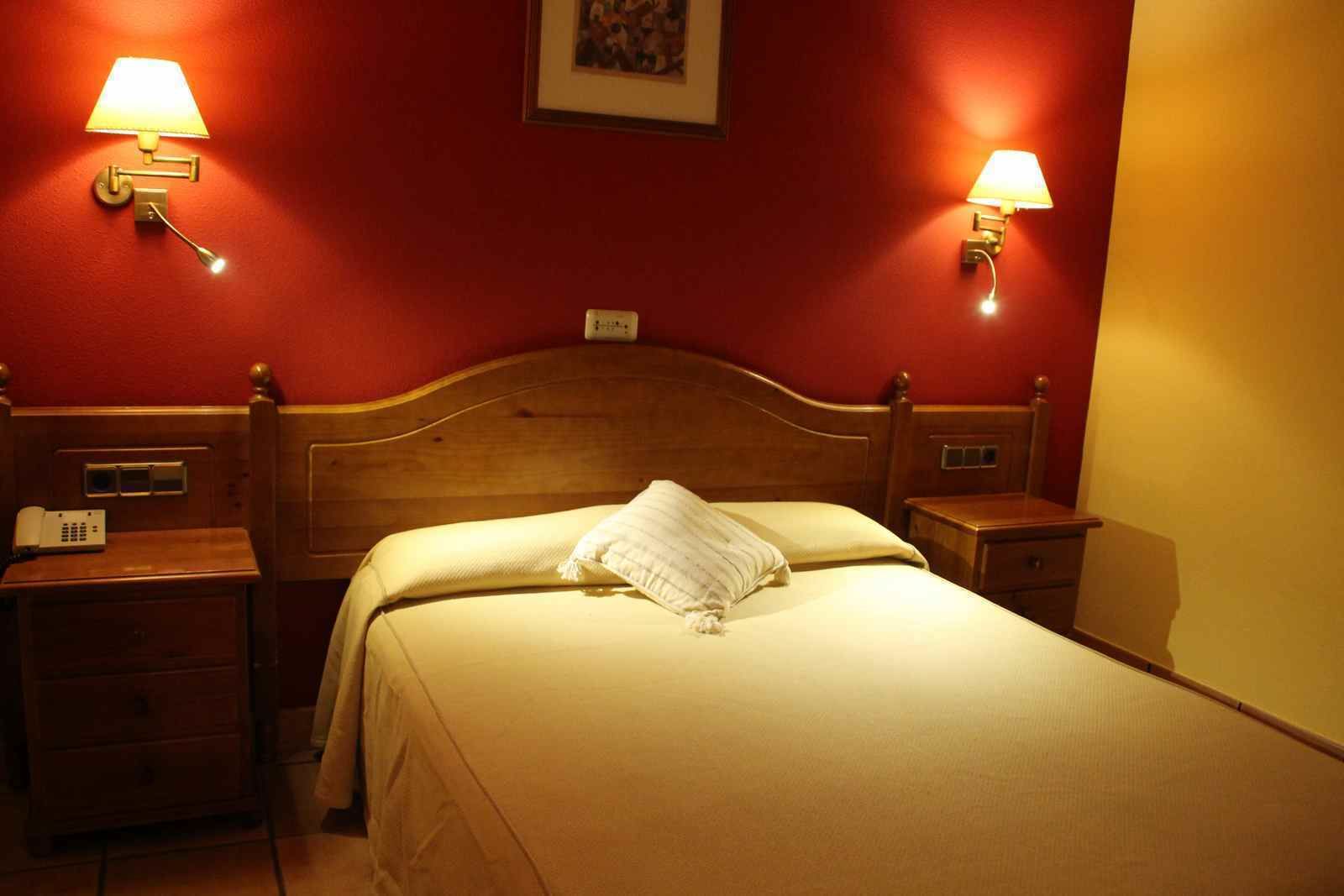 Ein Hotelzimmer mit einem hölzernen Kopfteil, zwei Nachttischen mit Lampen, einem Telefon und einem gerahmten Bild an der Wand.