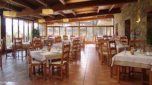 A restaurant with wooden tables and chairs, large windows, and stone walls.