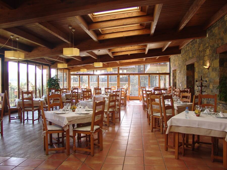 Un restaurante con mesas y sillas de madera, ventanas amplias y paredes de piedra.
