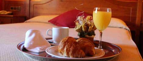 A breakfast tray with croissants, a glass of orange juice, and a white cup on a bed with a wooden headboard.
