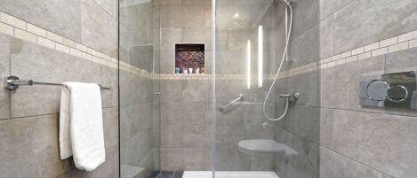 Une douche moderne avec une porte en verre, des toilettes blanches et un sol de douche carrelé.