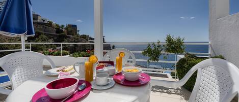 A table set with breakfast items on a balcony overlooking the sea.