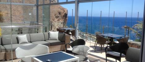 Un área de estar al aire libre con paredes de vidrio y vista al mar.