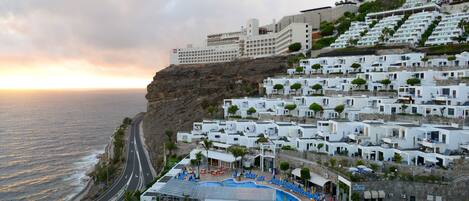 Un hôtel situé sur la côte, avec des bâtiments blancs, une piscine et une vue sur la mer.