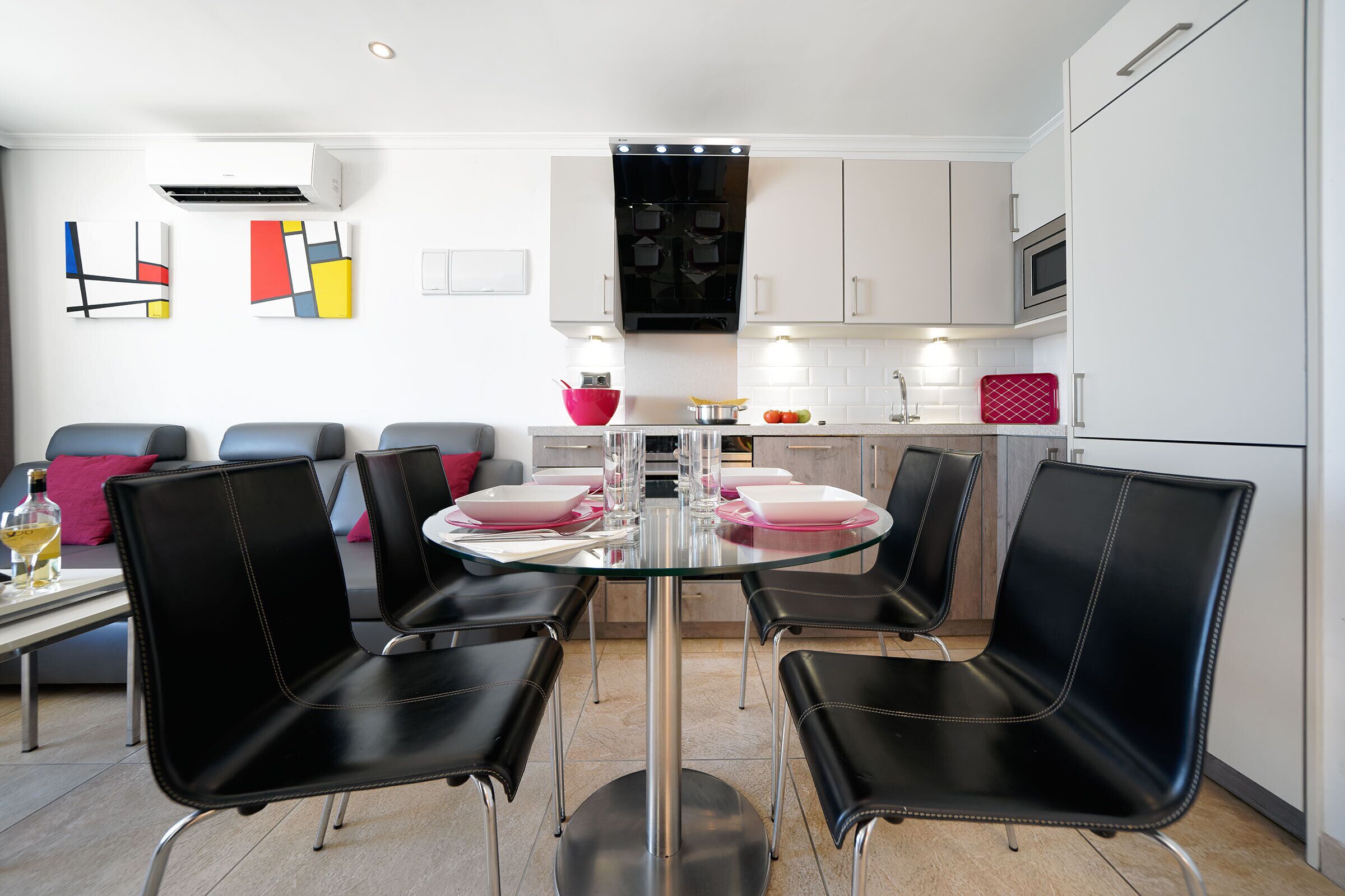 A modern kitchen with a glass dining table, black chairs, and white cabinets.