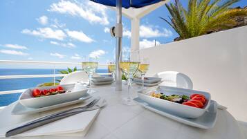 A table set for two with white plates, glasses, and cutlery, overlooking a coastal view.