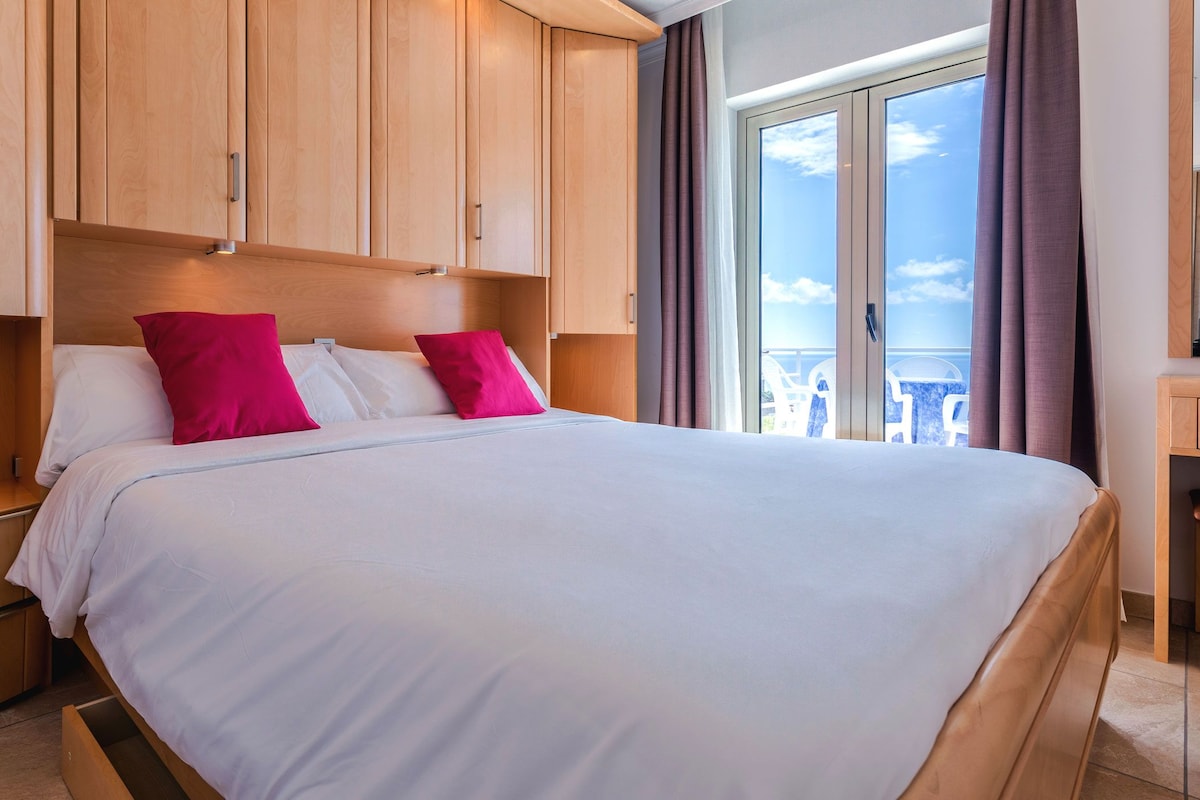 A hotel room with a bed, a nightstand, a wooden wardrobe, and a balcony with a view.