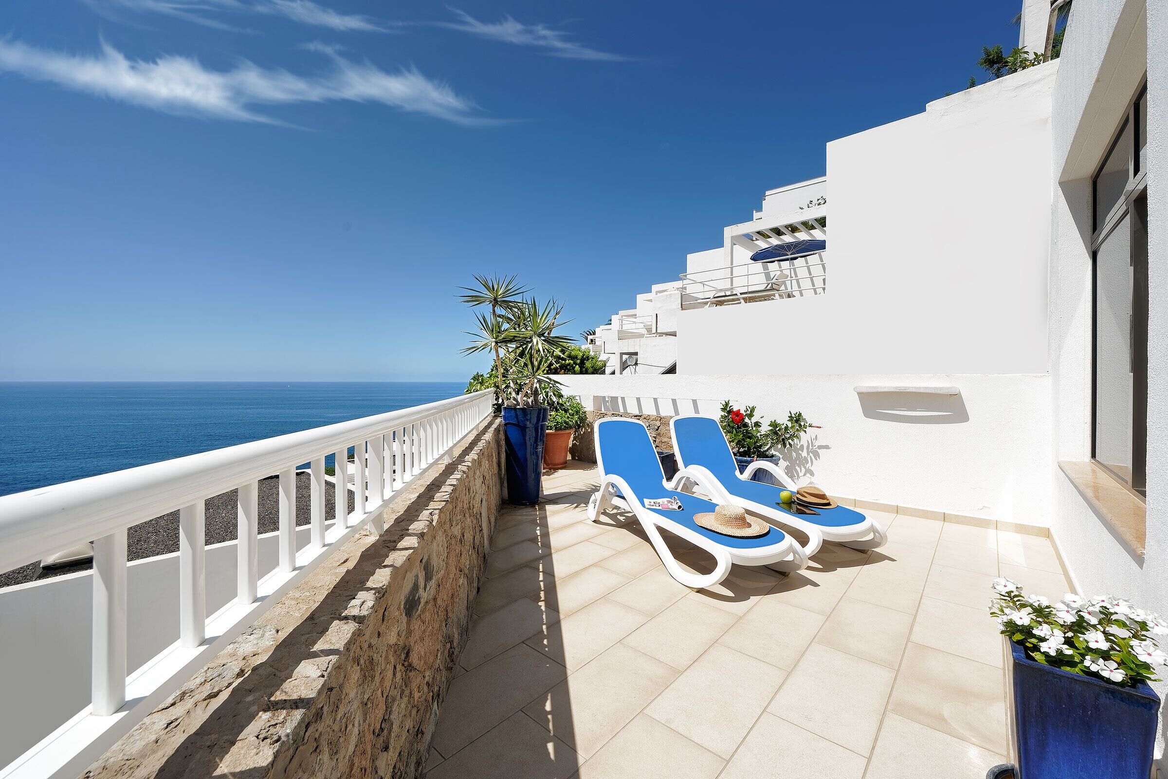 A balcony with two sun loungers, a potted plant, and a view of the sea.