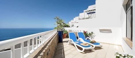 Un balcon avec deux chaises longues, une plante en pot et une vue sur la mer.