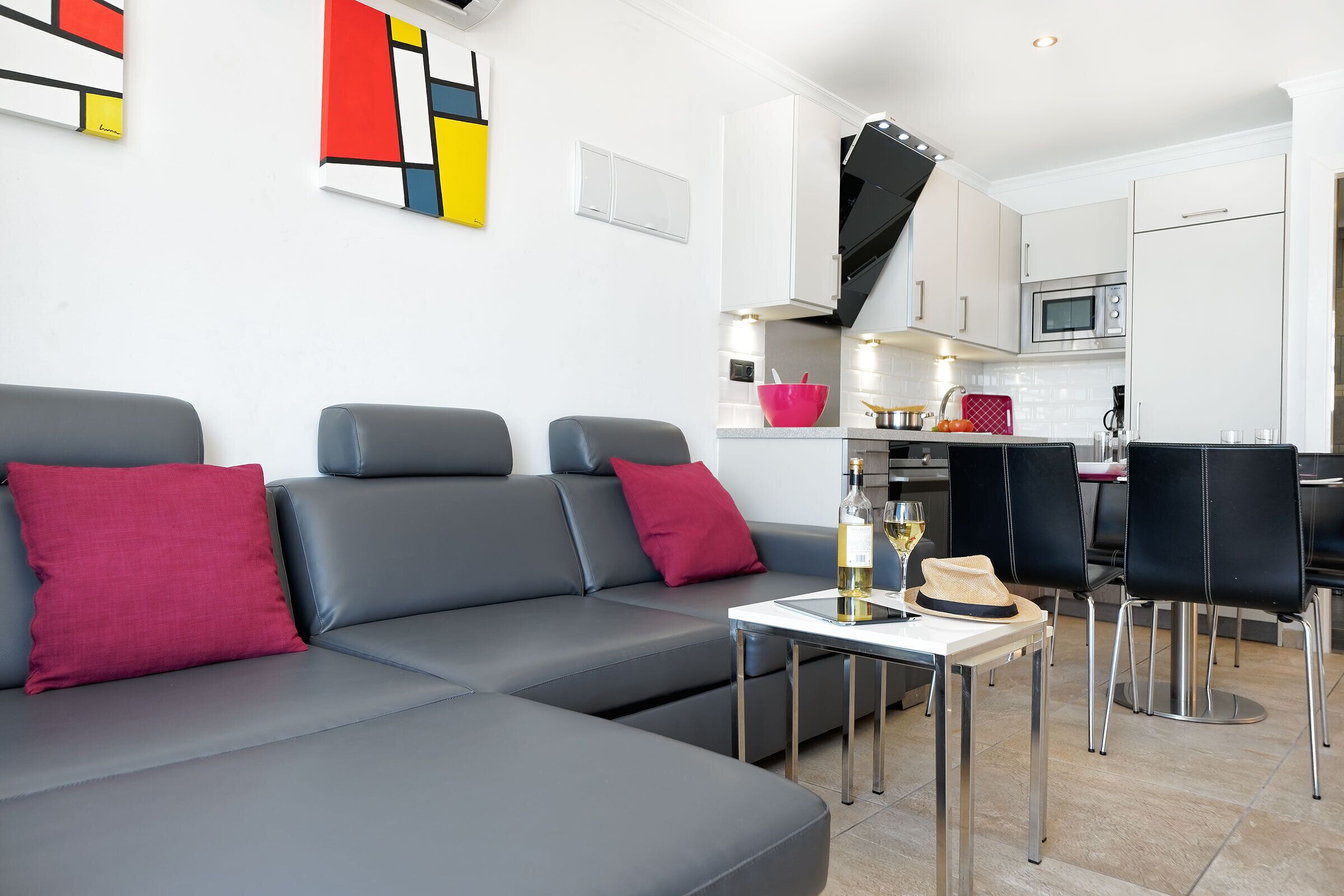 A modern living room with a grey sofa, red cushions, and a small table with a bottle and a hat.