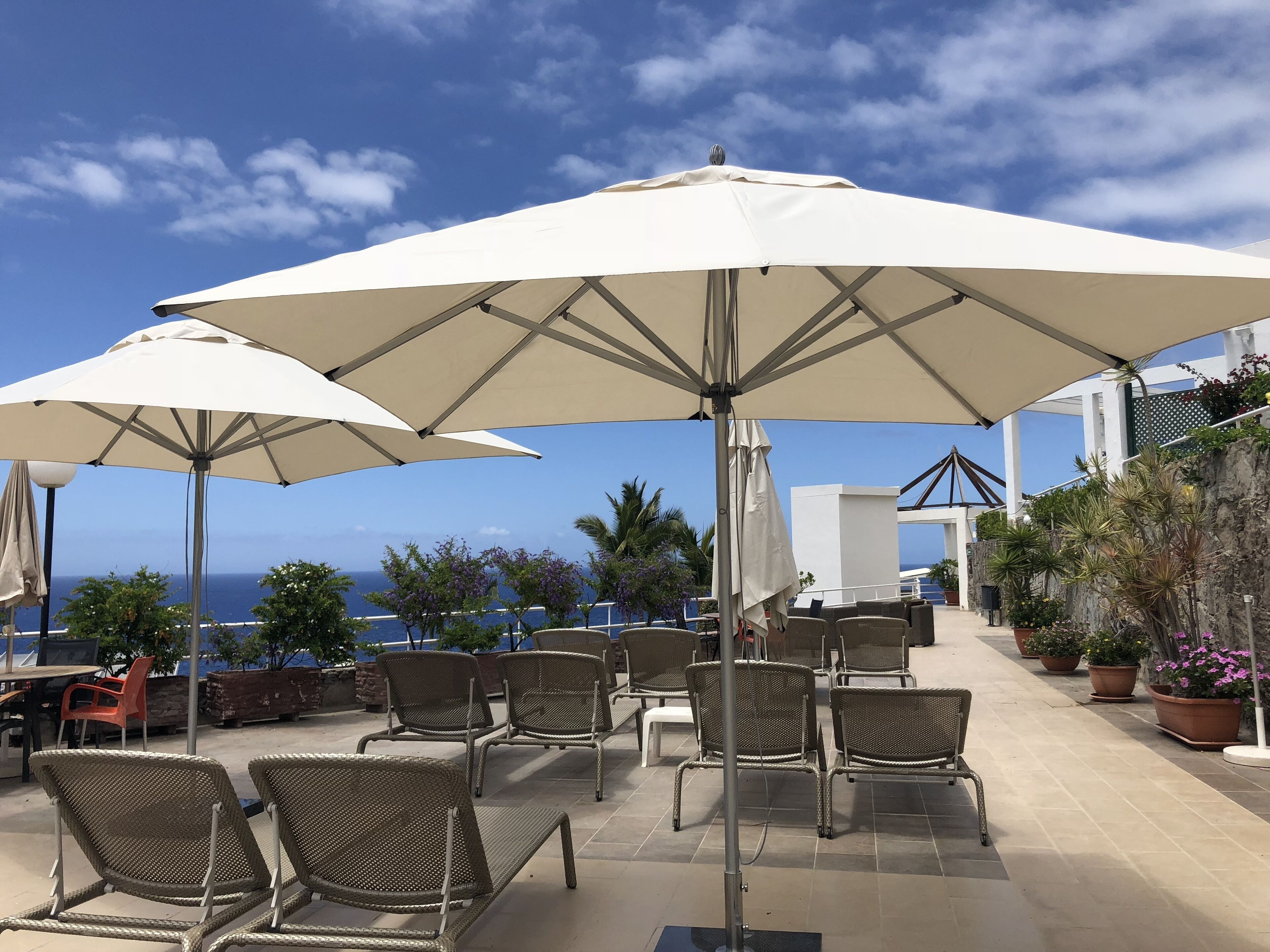 An outdoor seating area with wicker chairs and large umbrellas, overlooking a scenic ocean view.