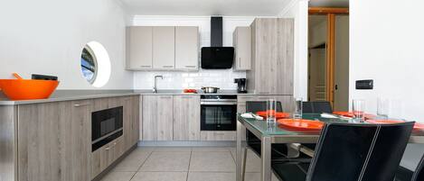 Une cuisine moderne avec des meubles en bois, un four encastré et un coin repas comprenant une table et des chaises en verre.