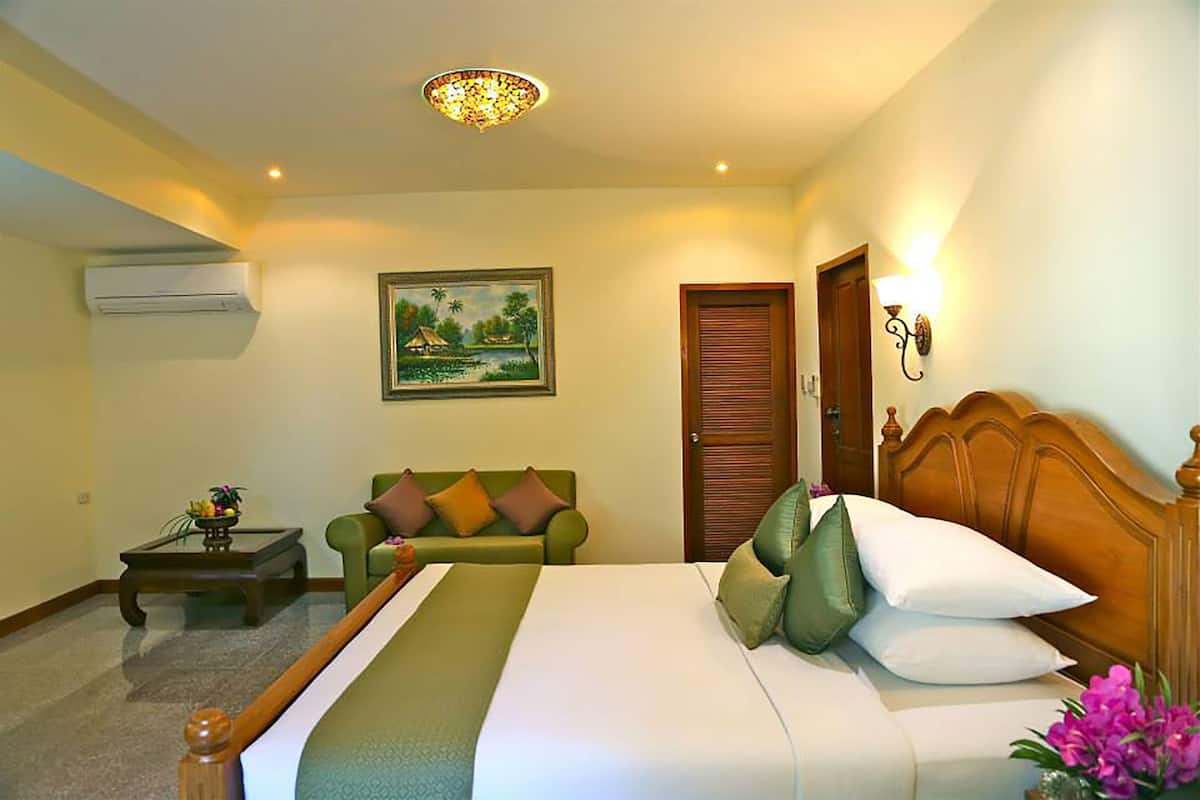 A hotel room with a bed, a green sofa, a wooden headboard, a painting on the wall, and a ceiling light fixture.
