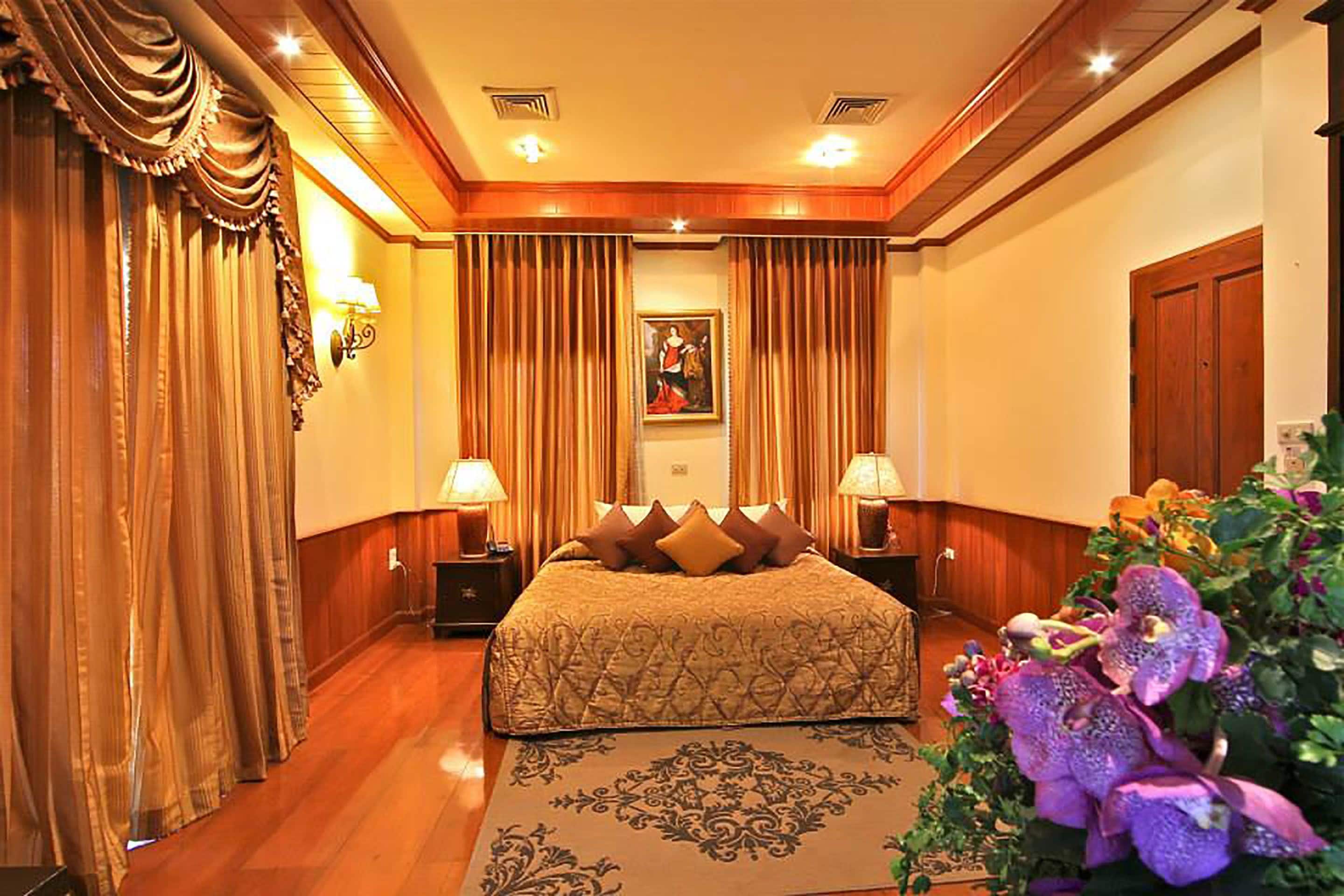 Habitación de hotel con una cama grande, dos lámparas de noche, un cuadro en la pared y un arreglo floral.