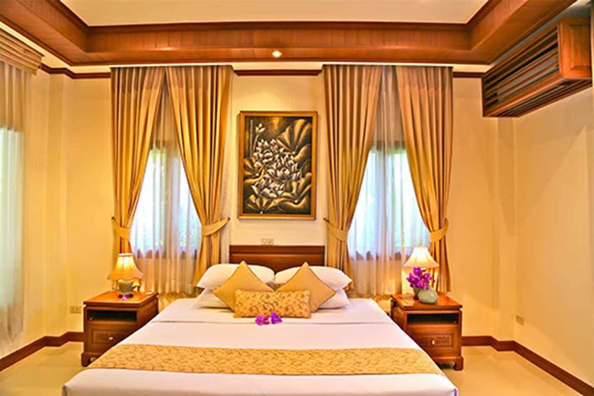 A large bed with a wooden headboard, two bedside tables with lamps, and a painting above the bed.
