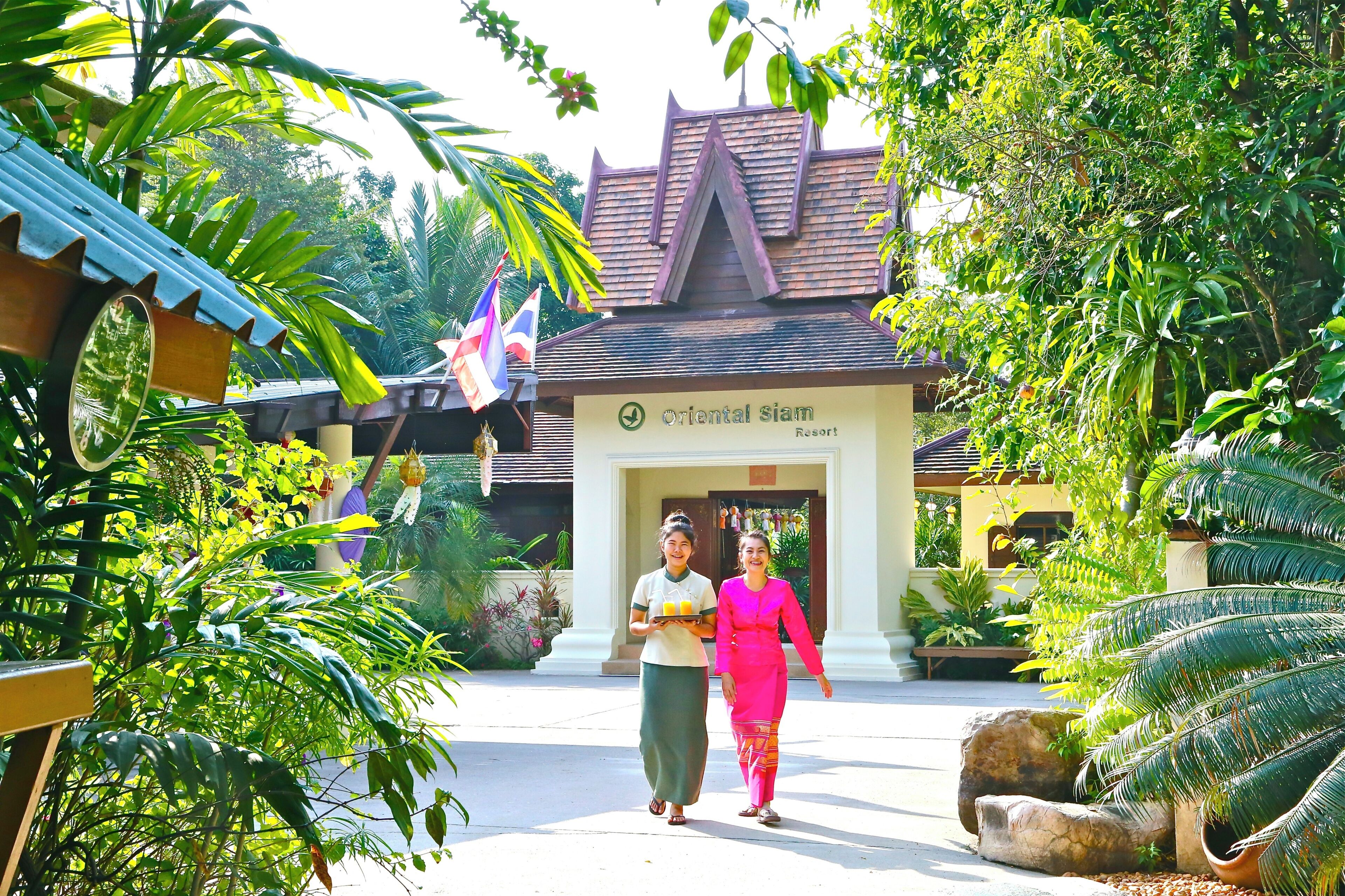Een gebouw met de naam 'Oriental Siam Resort', in traditionele bouwstijl, omringd door weelderige begroeiing en palmbomen.
