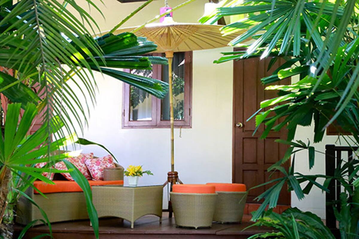 A cozy outdoor seating area with wicker furniture and a table, surrounded by lush greenery.