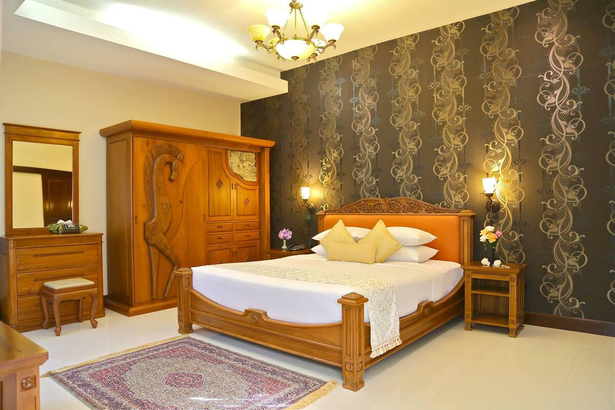 A bedroom with a large bed, wooden wardrobe, and a mirror.