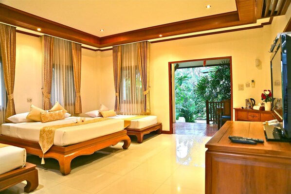 A hotel room with a large bed, a smaller bed, a desk with a remote control, and a view of greenery outside.