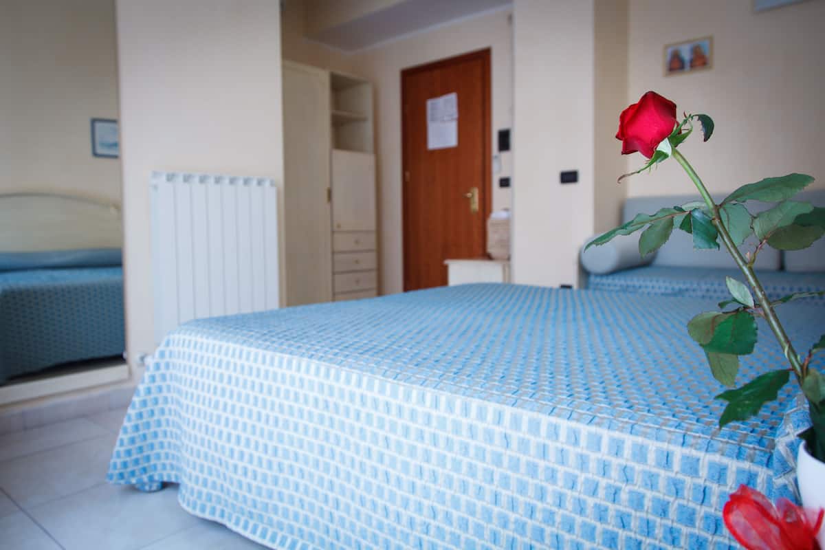 Une chambre avec une couvre-lit bleue à motifs, une rose rouge dans un vase blanc et une porte en bois en arrière-plan.
