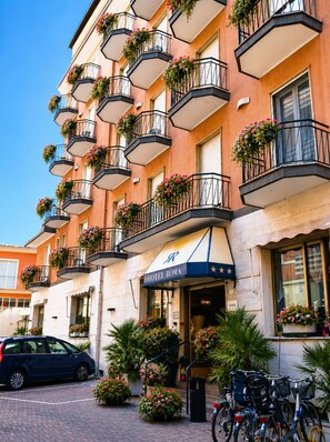 A multi-story hotel with balconies adorned with flower boxes, a clear sky, and a parked car.