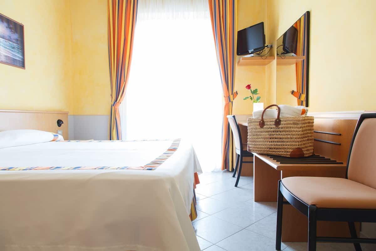 Une chambre d’hôtel avec un lit, un bureau et une chaise, une télévision et une fenêtre avec des rideaux.